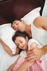 Daughter sleeping beside father on bed at home