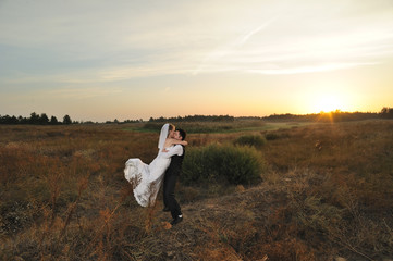 Obraz premium Bride and Groom in the Field at Sunset