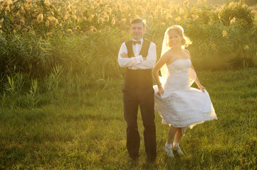 Naklejka na ściany i meble Bride and Groom having fun in the field filled with sunlight