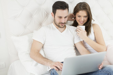 Fototapeta premium Young couple with laptop in the bed