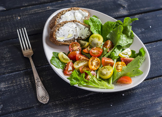 Fresh tomatoes and garden herbs salad and cheese sandwich on a white ceramic plate on dark wooden background. Delicious healthy food
