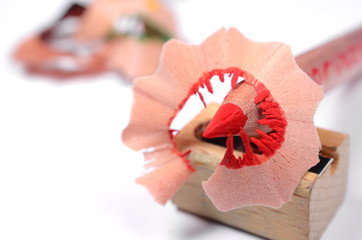 Bright red pencil with knife-sharpener and color wood shavings on a white background