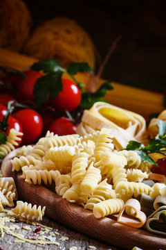 Italian food: pasta spiraline, herbs, tomatoes on old wooden bac