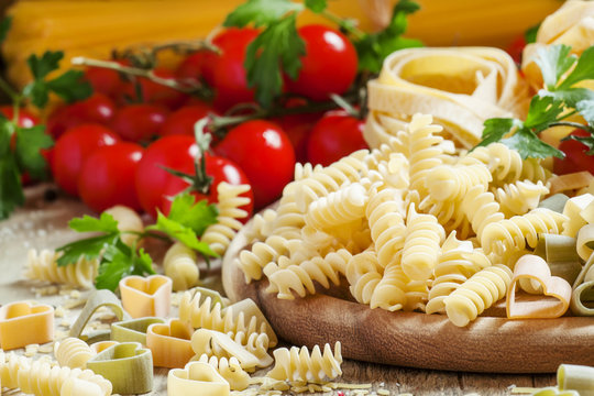 Italian food: pasta spiraline, herbs, tomatoes on old wooden bac