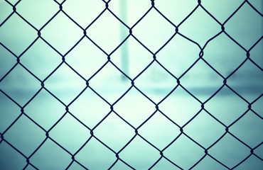 Fototapeta premium Outside abstract wire fence closeup with bright blue blurred background. 