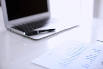 .Office workplace with a laptop and financial documents on the light reflecting table