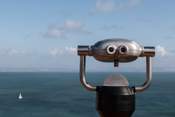 Sightseeing binoculars overlooking ocean with a sailboat in the distance.