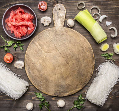 raw glass noodles, soy sauce, parsley, cherry tomatoes, onions, lettuce, mushrooms on a cutting board on wooden rustic background top view close up