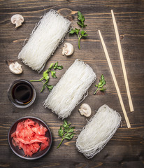 raw glass noodles with herbs, chopsticks, soy sauce and pickled ginger on wooden rustic background top view close up
