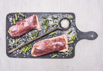Healthy foods two raw duck breast with rice and wooden spoon for the rice on a cutting board on wooden rustic background top view close up