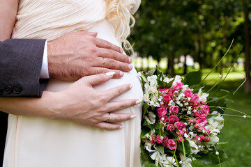 Obraz na płótnie Canvas Wedding couple hands with wedding ring on woman's pregnant belly
