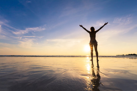 Young happy woman raising hands on a beautiful beach, sunset