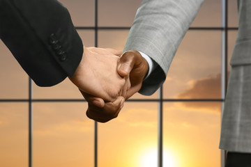 Businessmen shake hands beside window.