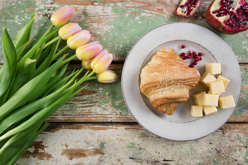 Fresh baked croissants with cheese on rustic wooden table. On the table are also tulips and pomegranate.