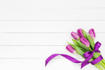 Bouquet of five tulips with ribbon bow on white wooden background. Top view, copy space