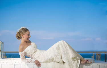 Fototapeta na wymiar Romantic beautiful bride in white dress posing on terrace with sea in background. Summer Wedding