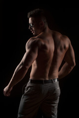 Fototapeta na wymiar back view of naked muscular man in pants on black