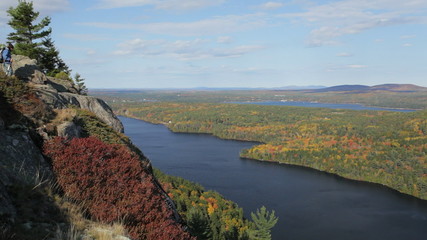 Hiker walking out to point and looking at Echo Lake and autumn foliage in Acadia National Park, Maine.