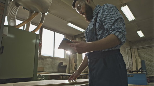 Young carpenter with the tablet quality control material. RAW video rcord.