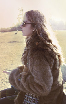 Jonge vrouw zit buiten op bankje met mobiele telefoon