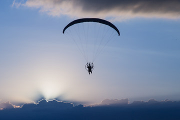 Silhouette paramotor / paraglider flying on sky.