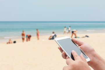 Naklejka premium Women using smartphone top on blurred blue sea and white sand be