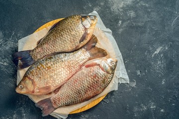 Three fresh carp on wooden board, top view, with copy space