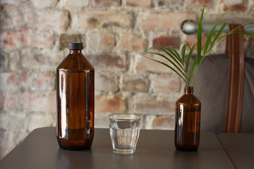 Glass bottle with water, the Brown bottle, a glass glass with water, a flower on a table