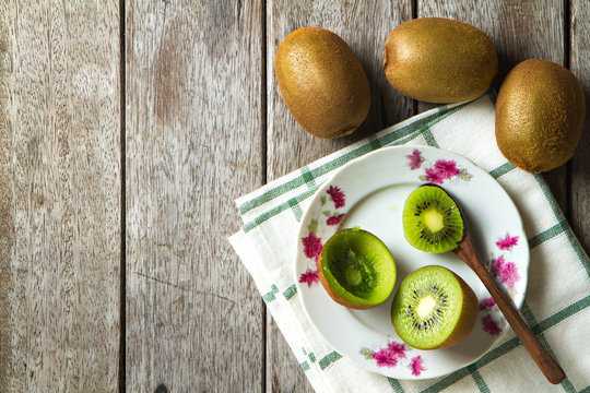 KIwi fruit on dish and spoon on wooden background.