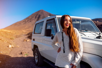 Young pretty woman dressed in sweater standing near the white jeep on the deserted and rocky landscape background  © rh2010