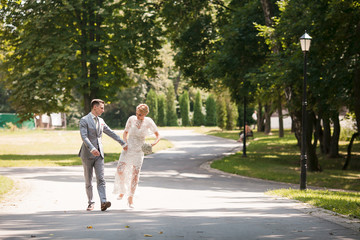 Fototapeta premium Bride and groom walking away in summer park outdoors