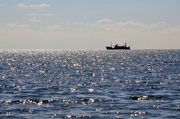 A ship floating on the sea on the horizon.