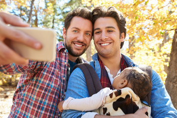 Gay Male Couple With Baby Taking Selfie On Walk In Woodland © Monkey Business