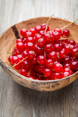 Redcurrant on a branch close to a wooden bowl.