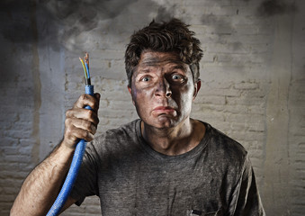 young man holding  cable smoking after electrical accident with dirty burnt face in funny sad expression
