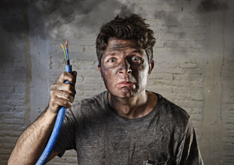 young man holding  cable smoking after electrical accident with dirty burnt face in funny sad...