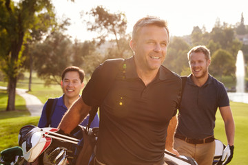 Group Of Male Golfers Walking Along Fairway Carrying Bags