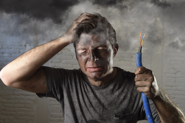 young man holding cable smoking after electrical accident with dirty burnt face in funny sad...