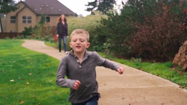 Little boy running down a path at a park while his mother follows, slow motion