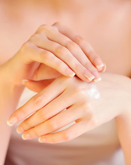 Young woman applies cream on her hands after bath. Focus on hand
