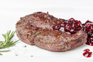 On a white plate delicious piece of tender steak, meat, served with cranberry sauce and spiced with rosemary, cherry tomato.