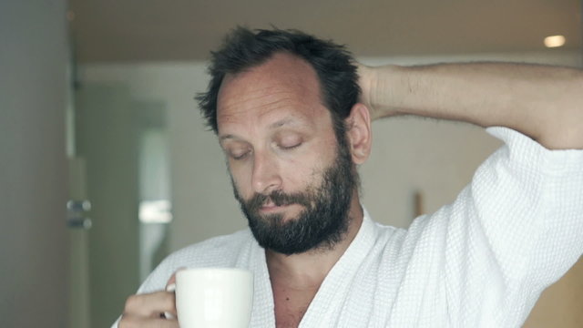Sleepy man in bathrobe drinking coffee in bathroom
