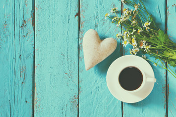 top view image of daisy flowers and fabric heart next to cup of coffee on blue wooden table
