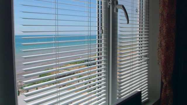 View from the open window with blinds on the sea in summer