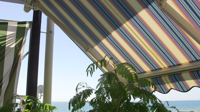 Terrace with retractable striped awnings with sea view in a sunny summer day closeup