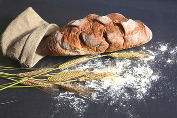 rustic crusty bread and wheat ears on a dark wooden table