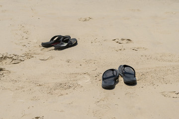 Black slippers on the sand beach background