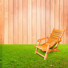 wooden deck chair on green grass with wooden wall background