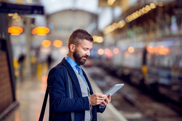 Hipster businessman with tablet, waiting, train platform
