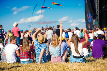 Teenagers, summer music festival, sitting in front of stage - obrazy, fototapety, plakaty